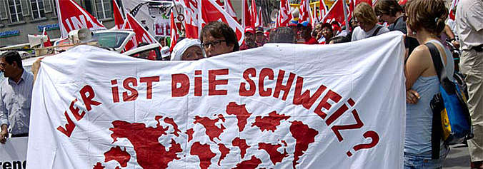 Auf dem Bild sind Menschen mit einem Transparent zu sehen. Darauf steht: Wer ist die Schweiz?
