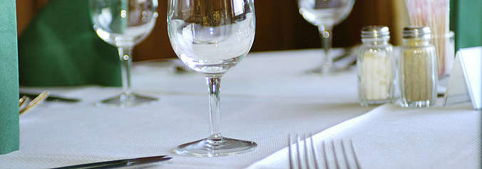 Auf dem Bild ist ein gedeckter Tisch mit Gläser, Besteck und Serviette zu sehen.