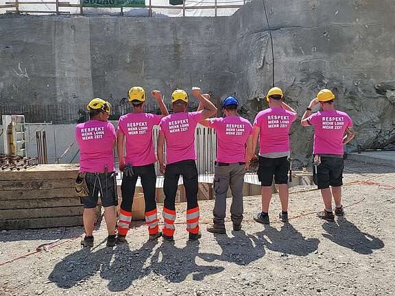  Eine Gruppe Bauarbeiter trägt Unia-Frauenstreik-T-Shirts mit der Aufschrift «Respekt, mehr Lohn, mehr Zeit» und zeigt geschlossen Haltung auf einer Baustelle.